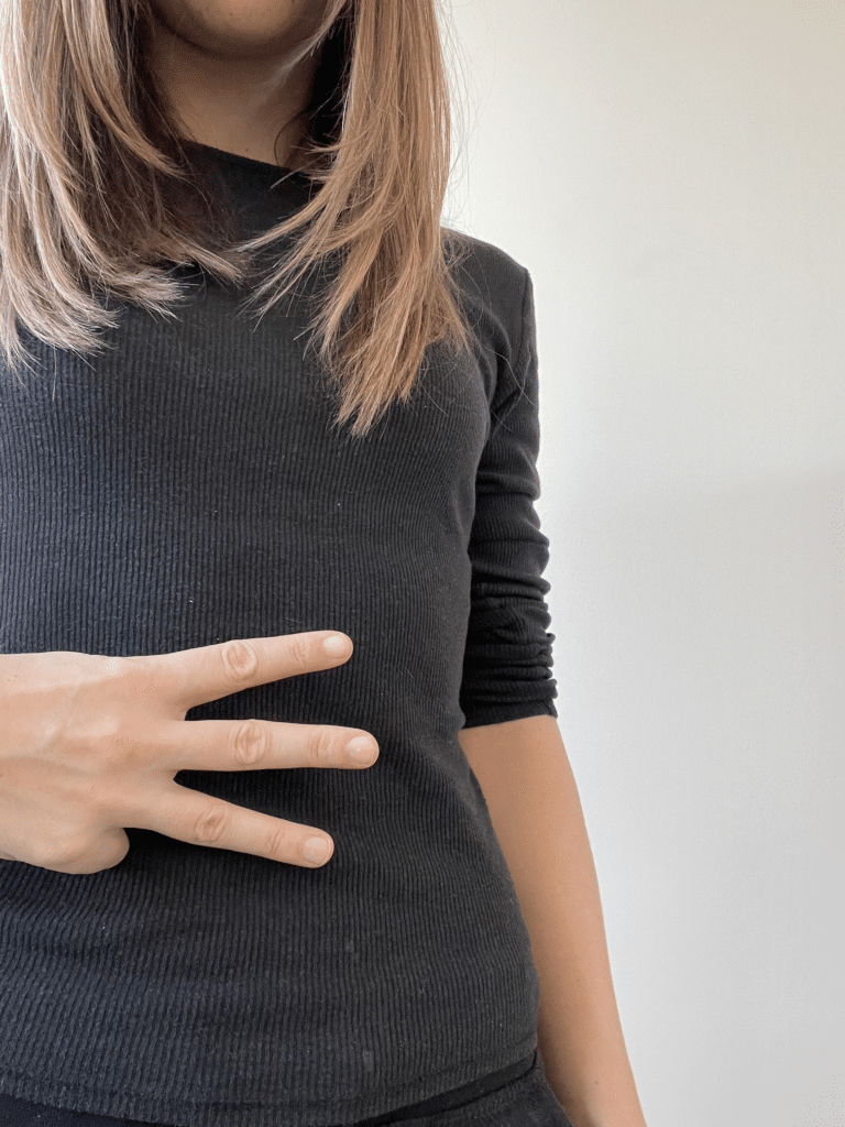 A woman is posing with her hands in front of her stomach, indicating potential stomach pain.
