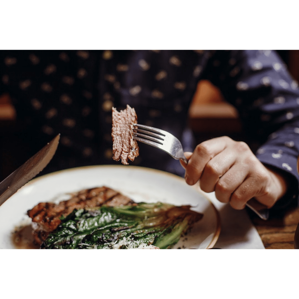 A person practicing naturopathy holding a fork while eating a steak during their ketogenic diet meal