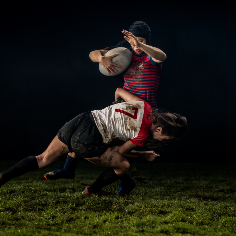 Two women playing rugby on a dark night, facing the risk of concussion.